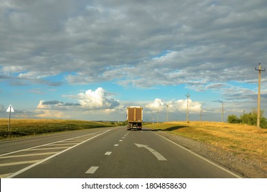 A Lone Van Truck Moving Away Along The Asphalt Road Outside The City Towards The Horizon. Beautiful Blue Sky With Lots Of Clouds.