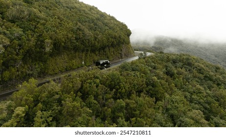 A lone vehicle travels along a winding road through a lush mountain landscape shrouded in mist, capturing the essence of adventure and tranquility. - Powered by Shutterstock