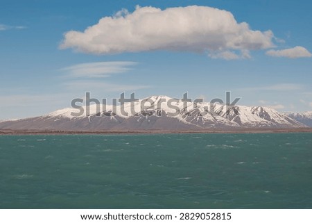 A lone white cloud drifting above vast snow‑dusted Patagonian peaks and turquoise waters (Calafate, Argentina: 12-sep-2011)