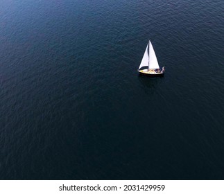 Lone white sailboat against the solid blue ocean.