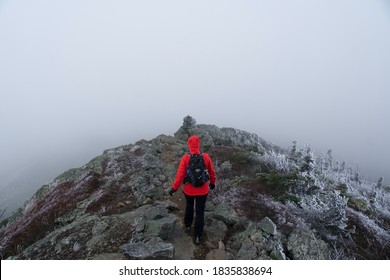 Lone Woman Hiking Over A Mountain Ridge On Icy Rocks In The Clouds