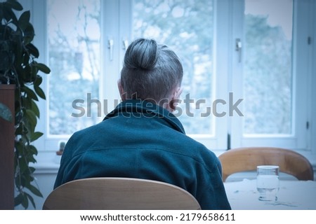 Loneliness concept, old-age depression: lonely old woman looking out of the window, blue filter effect.