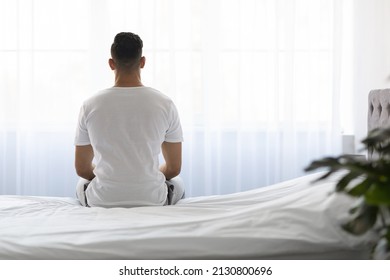 Loneliness Concept. Rear View Of Young Man Sitting On Bed And Looking At Window In The Morning, Unrecognizable Male In White T-Shirt Spending Time In Light Bedroom After Waking Up, Copy Space - Powered by Shutterstock