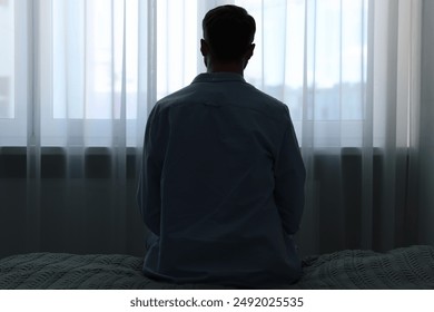 Loneliness concept. Sad man sitting on bed at home, back view