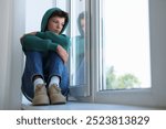 Loneliness concept. Sad teenage boy on windowsill indoors