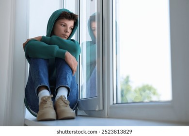 Loneliness concept. Sad teenage boy on windowsill indoors - Powered by Shutterstock