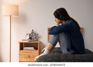 Loneliness concept. Sad teenage girl in headphones listening to music on bed at home - Powered by Shutterstock