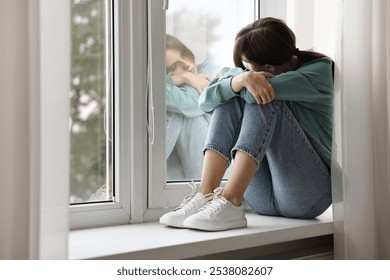 Loneliness concept. Sad teenage girl on windowsill at home - Powered by Shutterstock