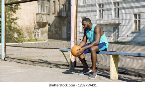 Lonely Afro-American sportsman sitting on bench and holding ball, depression - Powered by Shutterstock