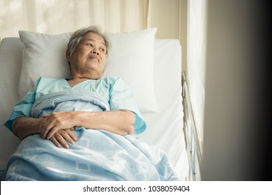 Lonely Asian Elderly Female Patient Lying On The Bed In The Hospital And Looking Away Outside The Window Waiting To See Her Child And Her Family To Visit.