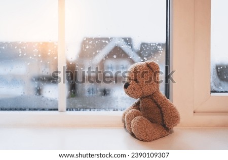 Lonely bear toy sitting alone looking out of window, Sad teddy bear doll sitting next to window in rainy day, Loneliness, Abuse concept, International missing Children day