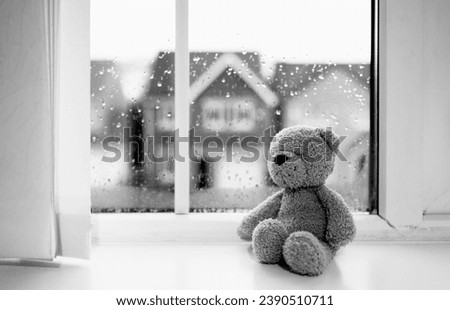 Lonely bear toy sitting alone looking out of window,Black and White Sad teddy bear doll sitting next to window in rainy day, Loneliness, Abuse concept, International missing Children day