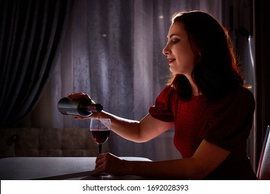 Lonely Beautiful Middle Aged Woman Alone In The Dark Kitchen Drinking Red Wine In The Evening Or Night. Concept Of Loneliness. Concept Of Pleasure. Drinking And Depression