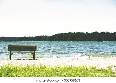 A lonely bench at the sea in the sand. Image has a vintage effect applied and the focus point is in the chair on the left.