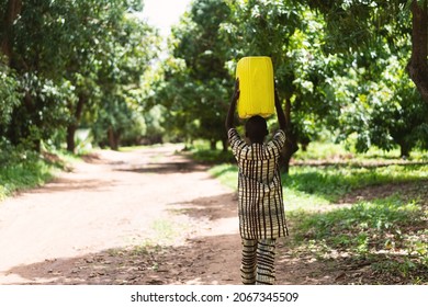 Lonely Black African Boy Walking On A Dirt Road With A Yellow Water Container On His Head