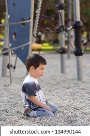 Lonely Bored Child Sitting On Ground In Playground.