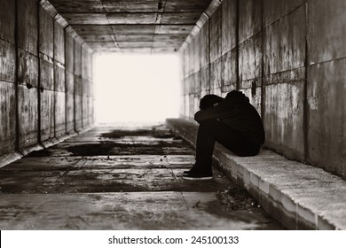 A lonely boy sits on a curb on the right side of a tunnel