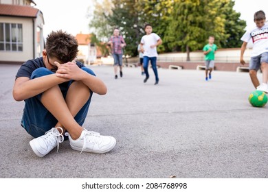 Lonely boy sitting alone on the ground, isolated from his peers