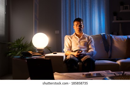 Lonely businessman at home sitting on sofa with hands clasped late at night.