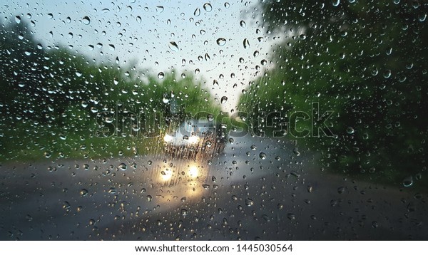 Lonely car with turn on\
headlights on a road through a defocused car window with raindrops.\
