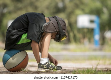lonely child with attitude of shame, guilt, boredom, sitting on a basketball while adults have fun on other less important things like watching their facebook