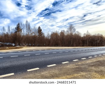 A lonely country road stretches alongside barren trees under a clear, partly cloudy sky on peaceful winter afternoon - Powered by Shutterstock