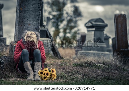 Lonely Crying Young Woman in Mourning with Sunflowers in front of a Gravestone in a Cemetery