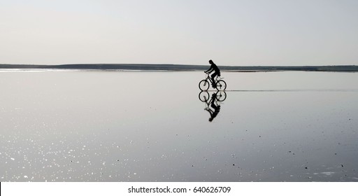 A Lonely Cyclist Riding By Still Water, Creating A Bewitching Mirror Illusion.