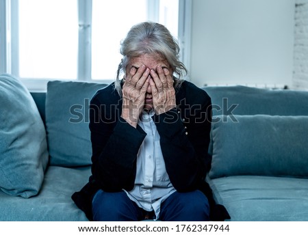 Lonely depressed senior old widow woman crying on couch in isolation at home, feeling sad and worried missing husband and family in COVID-19 Outbreak, lockdown, social distancing and Mental health.