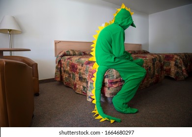 Lonely Dinosaur Man Sitting On The Edge Of The Bed In A Dark Motel Room