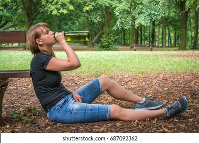 Lonely drunken woman holding a wine bottle in the park - alcoholism concept