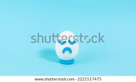 Lonely egg with a sad expression close up. The concept of a pessimistic outlook on life. Blue background. Сopy space. Close up.