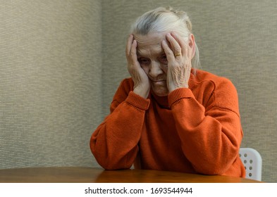 A lonely elderly woman sits at a table and holds her head sad from negative emotions