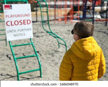 A Lonely Elementary School Aged Boy Looking At An Empty Playground Park Closed Due To Coronavirus Covid-19 And Reading A Closed Sign In Calgary, Canada