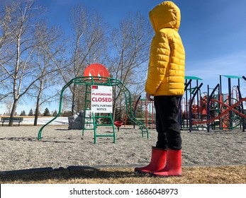 A Lonely Elementary School Aged Child Standing And Looking At An Empty Playground Park Closed Due To Coronavirus Covid-19 Sign In Calgary, Canada