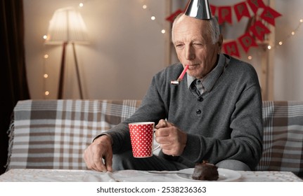 Lonely forgotten by children old man celebrating birthday alone at home. drinks tea and blows a whistle. Copy space - Powered by Shutterstock