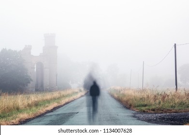 A lonely, ghostly figure walking down a foggy lane next to the ruins of an old castle. - Powered by Shutterstock