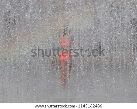 A lonely girl is crying among the refreshing splashes of a summer city fountain. Child carefree game in the rays of the rainbow during the summer holidays. Design of the improvement of the living mass
