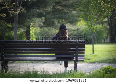 A lonely girl is sitting on a park bench. The face is hidden.