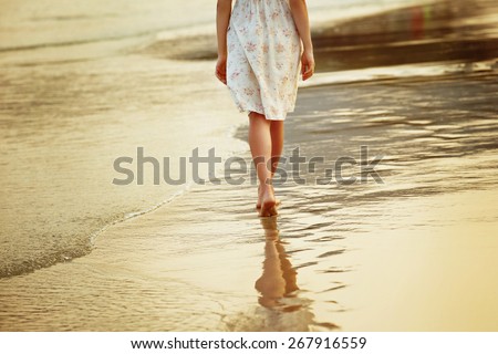 A lonely girl is walking along island coastline and has reflection on wet sand.