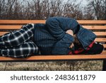 lonely homeless elderly old senior Caucasian man lying sleeping on a park bench in autumn