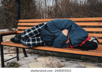 lonely homeless elderly old senior Caucasian man lying sleeping on a park bench in autumn
