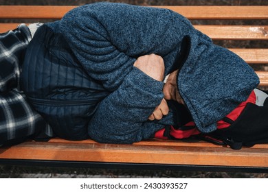 lonely homeless elderly old senior Caucasian man lying sleeping on a park bench in autumn