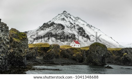 A lonely house at the foot of volcanic hill, in Arnarstapi, Iceland. In the background, we can see the Snaefellsjokull volcano. 