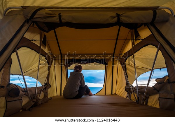 lonely independent strong middle age woman feeling\
the nature outdoor in a roof tent on the car. travel and lifestyle\
wanderlust concept for beautiful caucasian lady sitting in front of\
the ocean