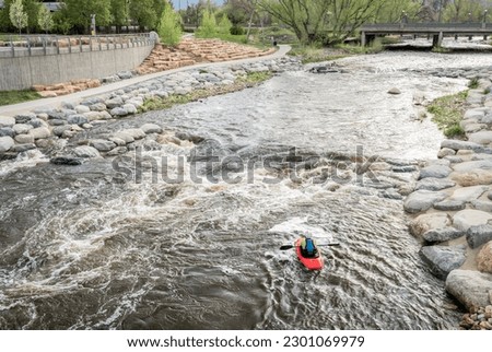 lonely kayaker surfing the wave in Whitewater Park on the Poudre River in downtown of Fort Collins, Colorado