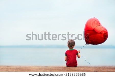 a lonely kid on the dock with a bright red balloon in the shape of a heart