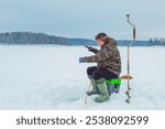 Lonely man fishes in an ice hole on a winter lake. Winter fishing, ice fishing. Hobby, winter free time concept.