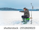 Lonely man fishes in an ice hole on a winter lake. Winter fishing, ice fishing. Hobby, winter free time concept.