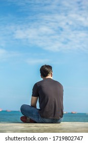 Lonely man guy sitting on the concrete floor looking at the blue sea with blue sky background